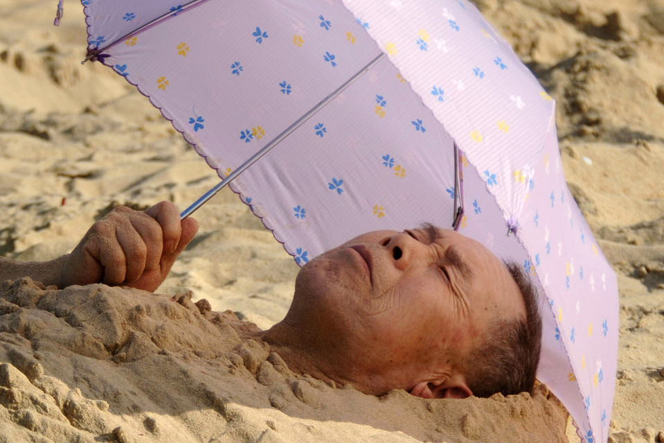 Отдыхающий мужчина закопал себя в песке на пляже реки Наньду в Хайкоу, провинция Хайнань, Китай. (ZUMA Press / Xinhua)